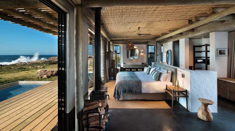 Suíte do GweGwe Beach Lodge com portas de vidro abertas para deck com piscina; vista do Índico e ondas na costa de Mkambati (Wild Coast, África do Sul). GweGwe Beach Lodge, África do Sul