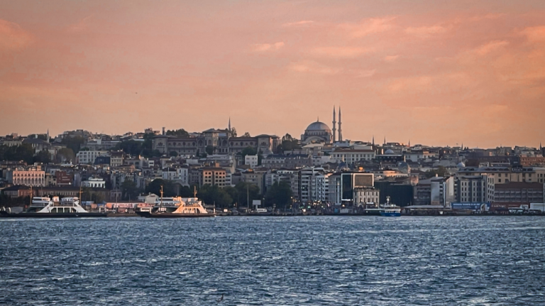 Skyline de Istambul ao entardecer, visto da água, com ferries em primeiro plano e uma grande mesquita destacada no alto da cidade Vista de Istambul ao entardecer, com o mar em primeiro plano e o skyline histórico ao fundo