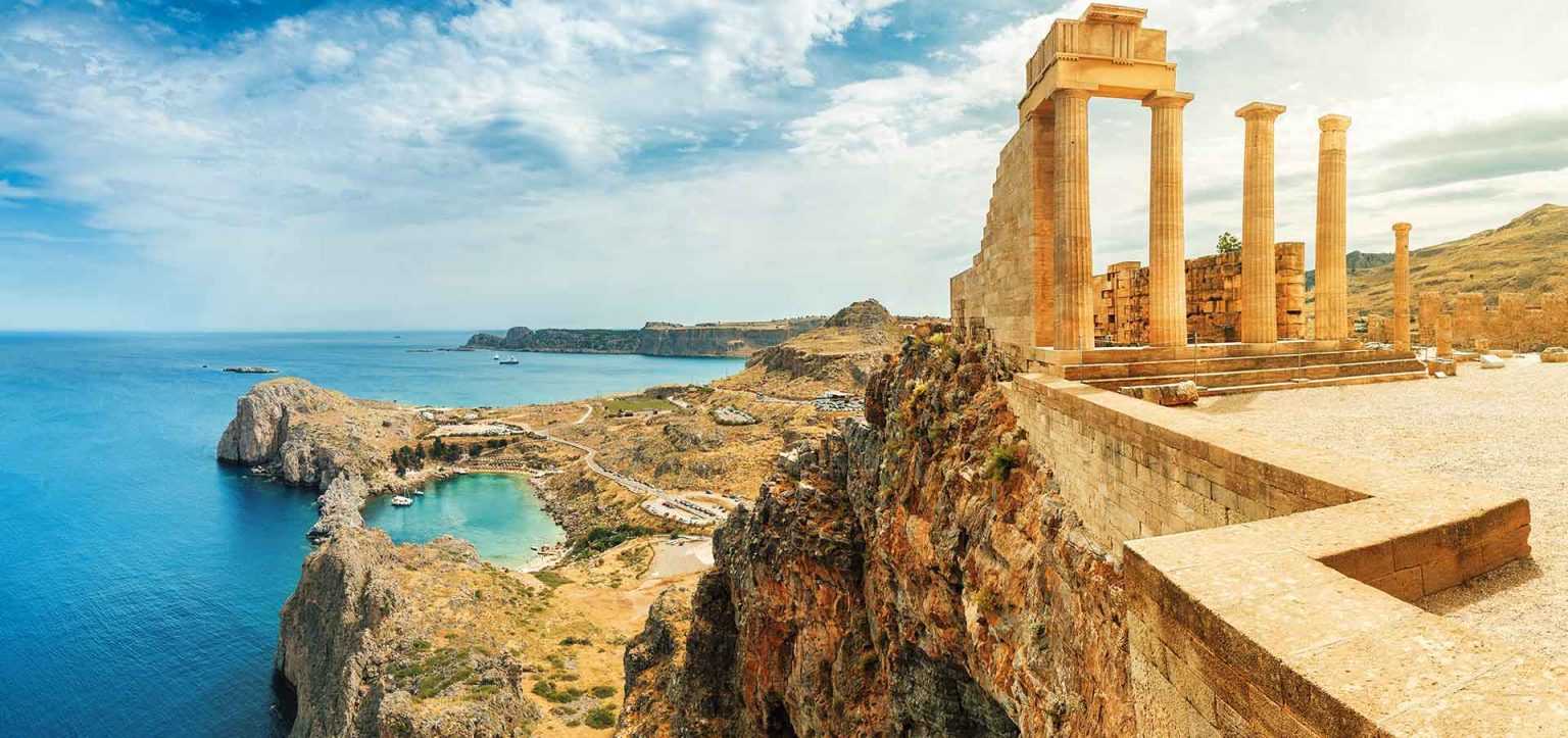 Acrópole de Líndos (Rodes): ruínas dóricas e muralhas medievais no topo do penhasco, vila caiada e baías azul-turquesa do mar Egeu ao fundo.