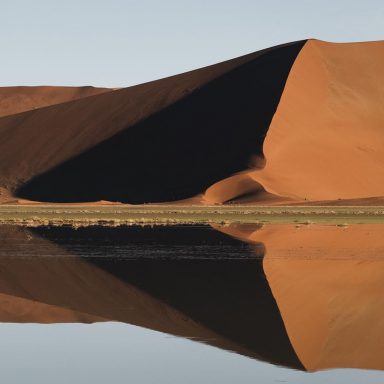Vista panorâmica do Deserto do Namibe, na Namíbia, com mar de dunas vermelhas ondulantes sob céu azul.