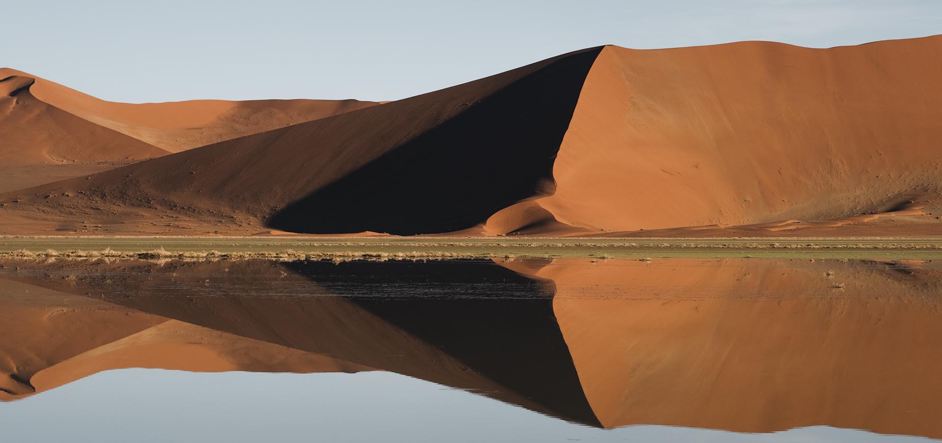 Vista panorâmica do Deserto do Namibe, na Namíbia, com mar de dunas vermelhas ondulantes sob céu azul.