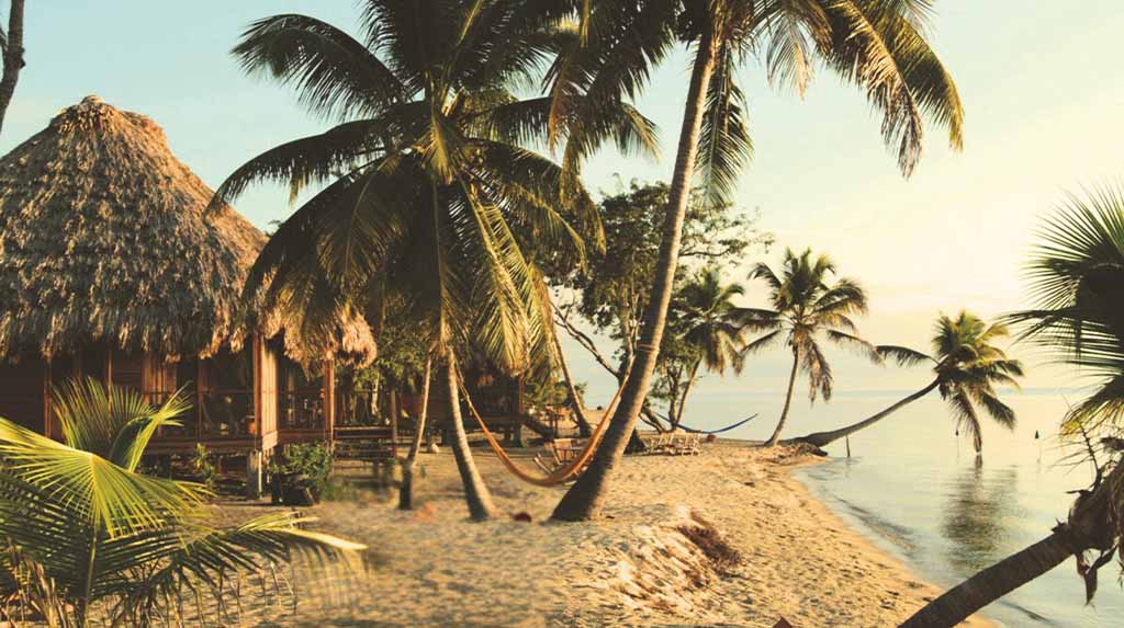 Bangalôs de palha e coqueiros na praia em Placencia, Belize, refúgio de viagem que combina Rota Maia e descanso à beira-mar