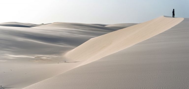Silhueta de uma pessoa no topo de uma duna isolada, capturando a sensação de imensidão e perda de perspectiva no Parque Nacional dos Lençóis Maranhenses.