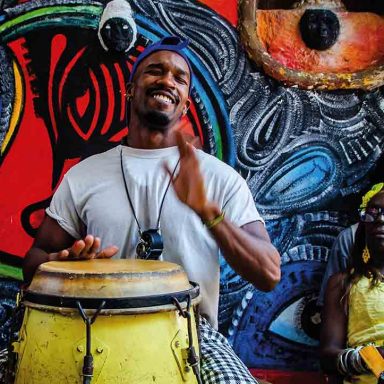 Roda de música afro-cubana em Havana, Cuba, com percussionista sorrindo, clima de noite animada e dica cultural de o que fazer na viagem