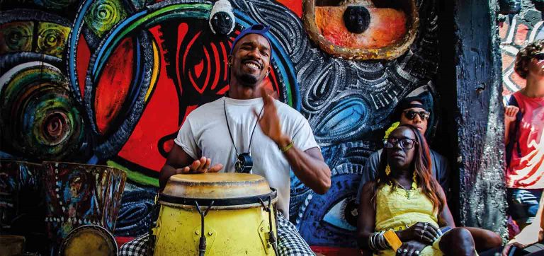 Roda de música afro-cubana em Havana, Cuba, com percussionista sorrindo, clima de noite animada e dica cultural de o que fazer na viagem