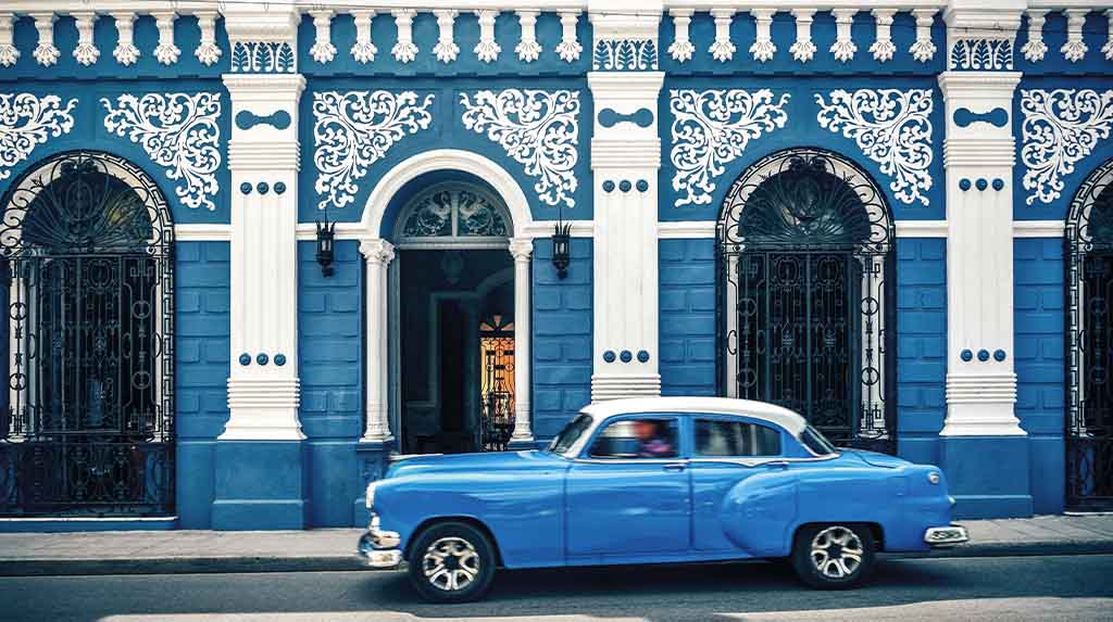 Carro antigo azul passando diante de fachada azul colonial em Havana, Cuba, imagem típica de roteiro fotográfico pela cidade