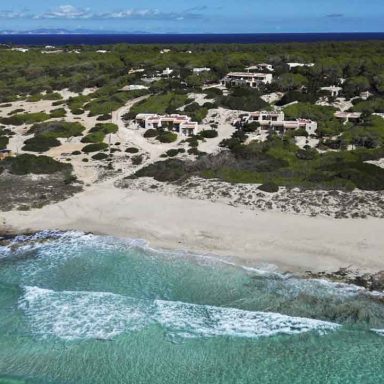 Vista aérea do Dunas de Formentera, mostrando bangalôs integrados à paisagem costeira de vegetação nativa, com a praia de areia clara e o mar Mediterrâneo turquesa.