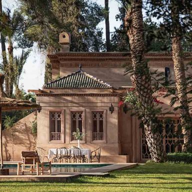Arquitetura do Jnane Rumi e jardins com palmeiras, área de refeição externa e piscina. Acomodação de luxo Marrakesh.