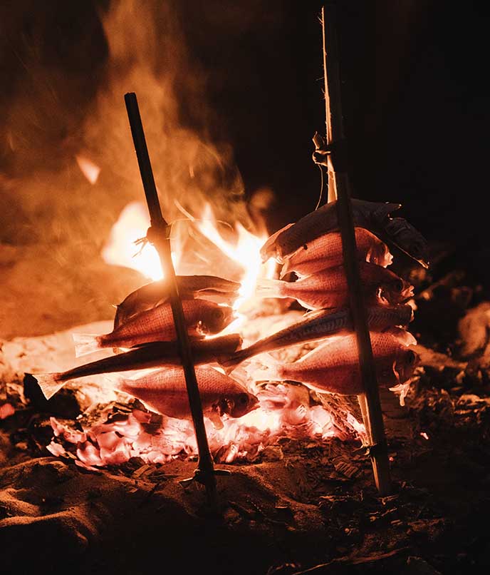 Preparo tradicional de peixe assado na brasa em espetos de madeira, culinária típica da cultura Mahoca em Benguerra.
