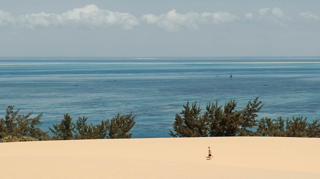 Vista panorâmica do alto da duna da Ilha de Bazaruto, exibindo o mar em múltiplas tonalidades de azul e o horizonte do Oceano Índico.