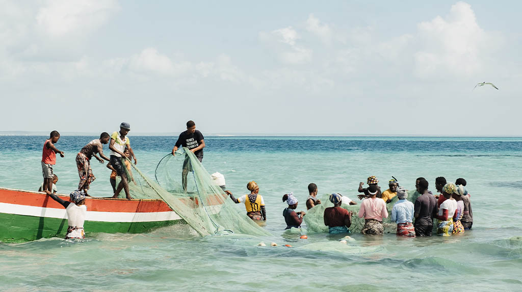Pescadores da comunidade Mahoca recolhendo redes de pesca artesanal em barco colorido no mar turquesa da Ilha de Benguerra, Moçambique.