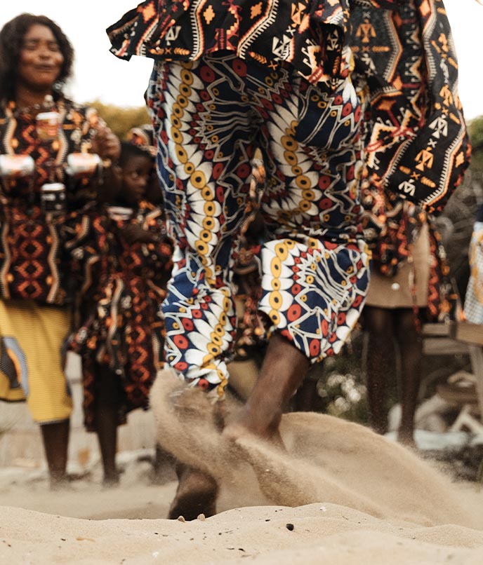 Detalhe dos pés e trajes estampados coloridos de moradores locais durante dança tradicional Mahoca na areia da Ilha de Benguerra.