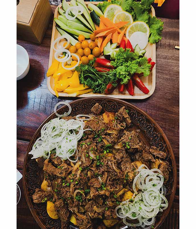 Prato tradicional quirguiz à base de carne de cordeiro com cebolas e especiarias, acompanhado de legumes frescos e ervas, servido em mesa típica