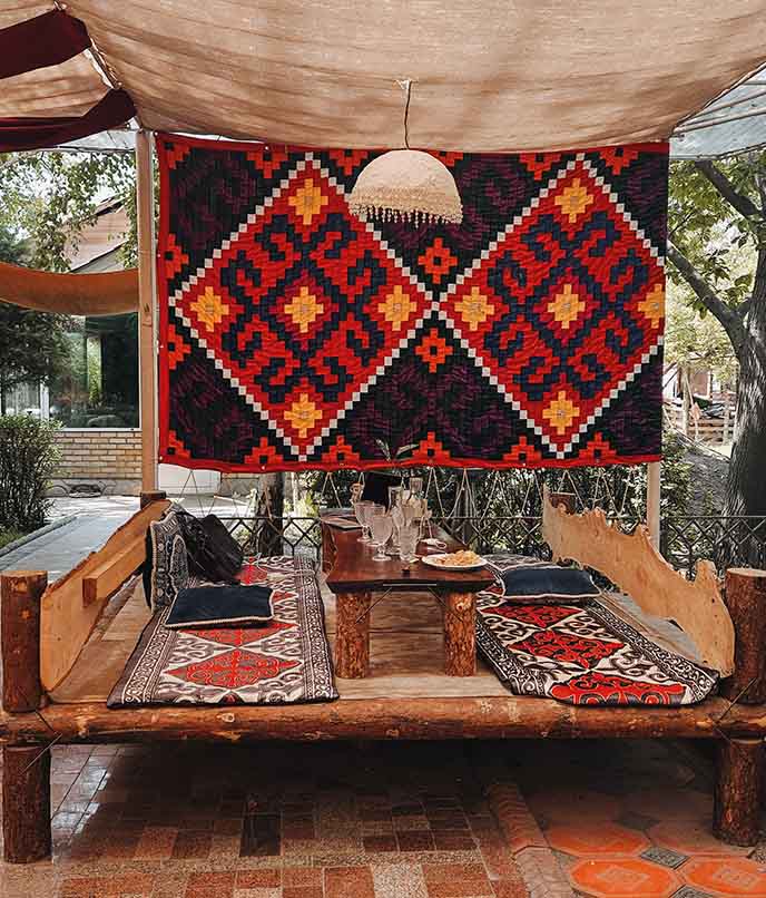 Espaço tradicional quirguiz com tapetes coloridos, mesa baixa e decoração têxtil, usado para refeições típicas em Bisqueque