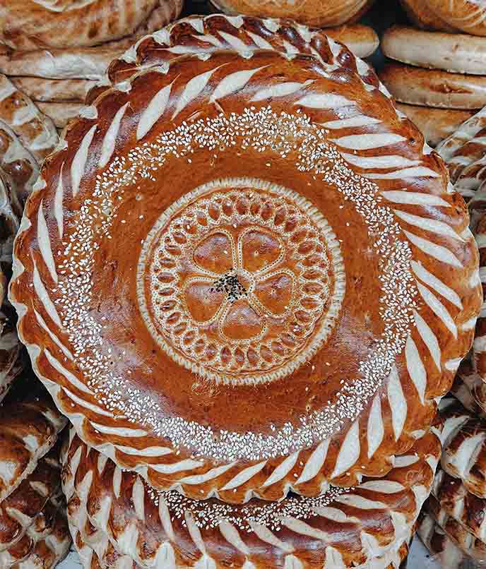 Pão tradicional quirguiz do Osh Bazar, redondo e decorado, com gergelim e motivos simbólicos da Ásia Central