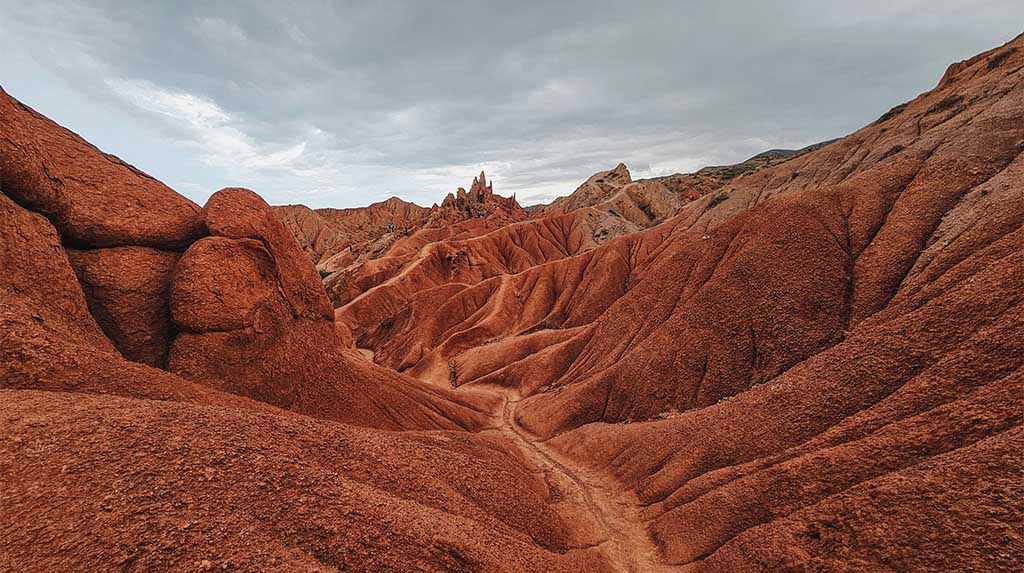 Formações rochosas avermelhadas do Mars Canyon, no Quirguistão, com ravinas sinuosas e relevo esculpido pela erosão