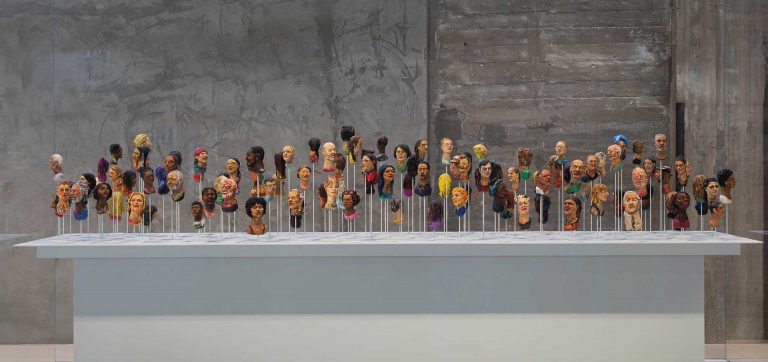 Instalação artística com múltiplos bustos coloridos e de etnias diversas, representando a condição humana e a diversidade. Arte contemporânea Fenix Museum.