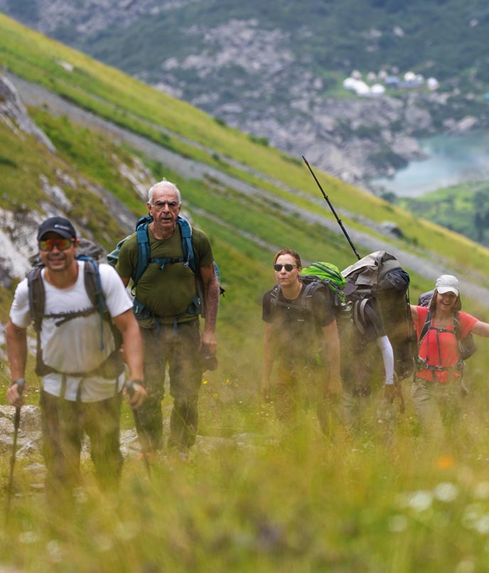 Grupo de viajantes realizando trekking nas montanhas do Quirguistão, com vales verdes e lago alpino ao fundo, região de Ala-Kul
