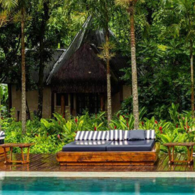 Piscina da Fazenda Shanti na Chapada dos Veadeiros, com camas de descanso de madeira e palmeiras cercadas por vegetação tropical