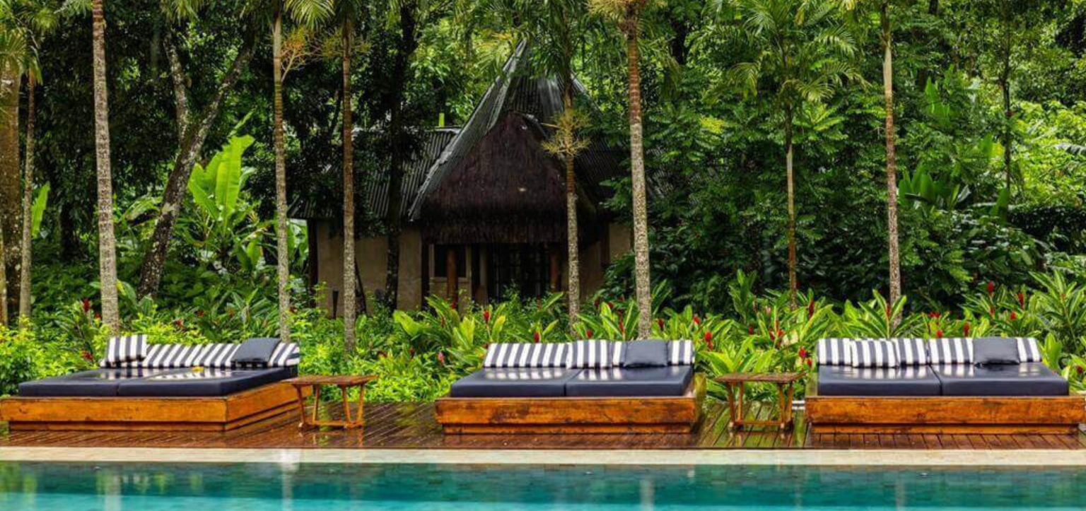Piscina da Fazenda Shanti na Chapada dos Veadeiros, com camas de descanso de madeira e palmeiras cercadas por vegetação tropical