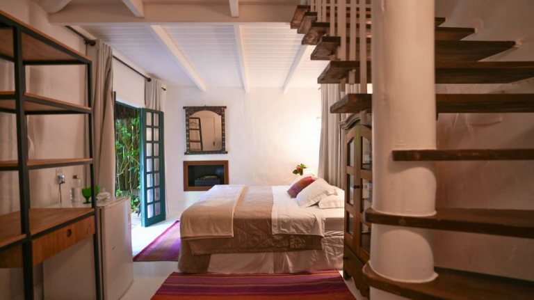 Suíte de chalé na Fazenda Shanti, Chapada dos Veadeiros, com cama king, porta aberta para o jardim e decoração rústico-chique Suíte da Fazenda Shanti