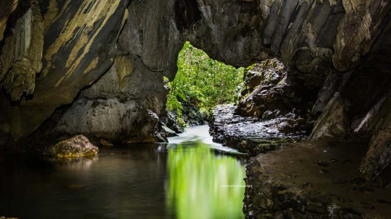 Interior de caverna com riacho e reflexo verde na entrada, no PETAR, Vale do Ribeira, Brasil.