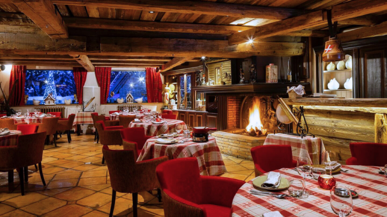 Restaurante Saint-Nicolas do Hôtel Le Lana (Courchevel 1850), com lareira acesa, madeira aparente e mesas xadrez em estilo savoyard. Restaurante Saint-Nicolas do Hôtel Le Lana (Courchevel 1850)