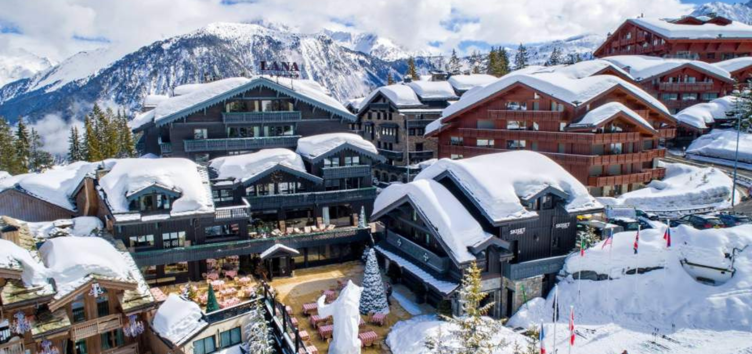 Vista aérea do Hôtel Le Lana, em Courchevel 1850 (Alpes franceses), com chalés cobertos de neve e montanhas ao fundo.