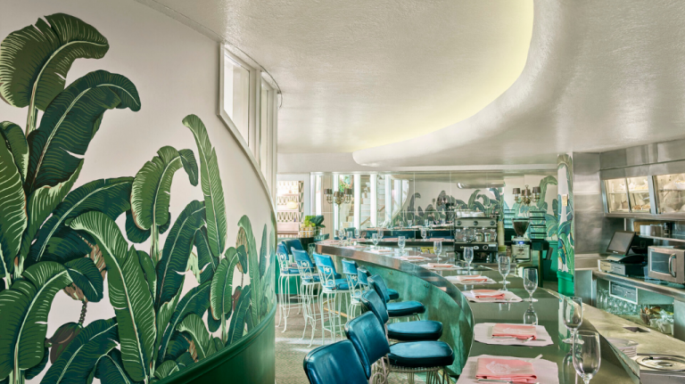 Interior do The Fountain Coffee Room no The Beverly Hills Hotel, com balcão curvo e mural de folhas de bananeira — cenário clássico de Beverly Hills ligado ao legado de Paul R. Williams