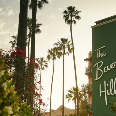 Letreiro verde do The Beverly Hills Hotel entre palmeiras ao entardecer, em Beverly Hills, Los Angeles — ponto de partida do tour Building Dreams in Beverly Hills inspirado em Paul R. Williams.”