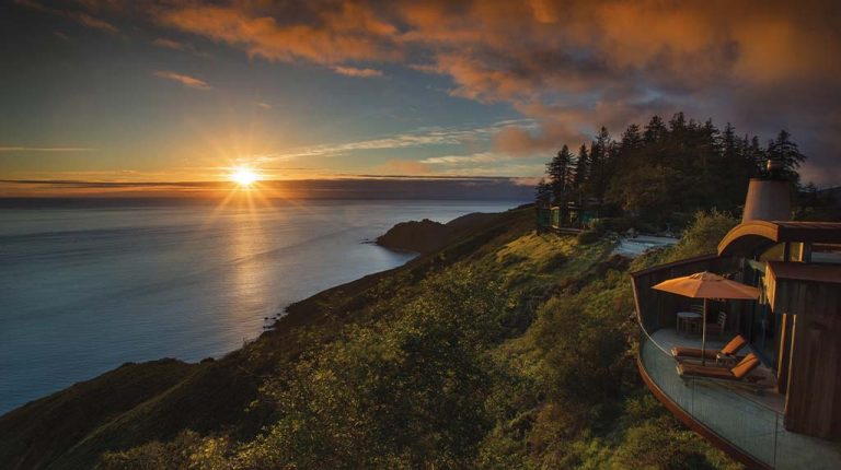 Varanda privativa de suíte no Dunas de Formentera com mesa de madeira, tons terrosos e vista desimpedida para o mar Mediterrâneo turquesa.