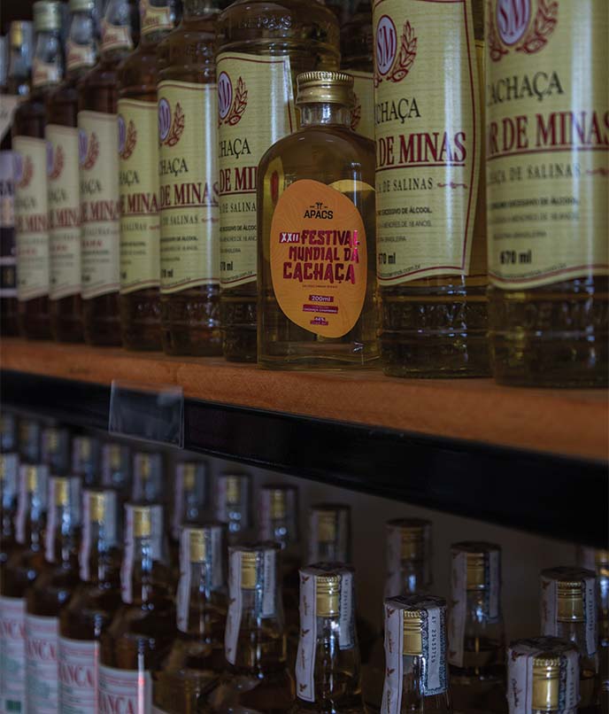 Garrafas de cachaça de alambique em prateleira durante roteiro cultural por Minas Gerais, com foco em tradição, memória e produção artesanal.