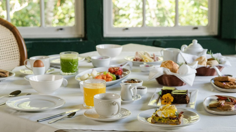 Mesa de café da manhã no restaurante Pau e Pedra, do Ronco do Bugio, em Piedade, com pratos servidos em ambiente cercado pela Mata Atlântica.
