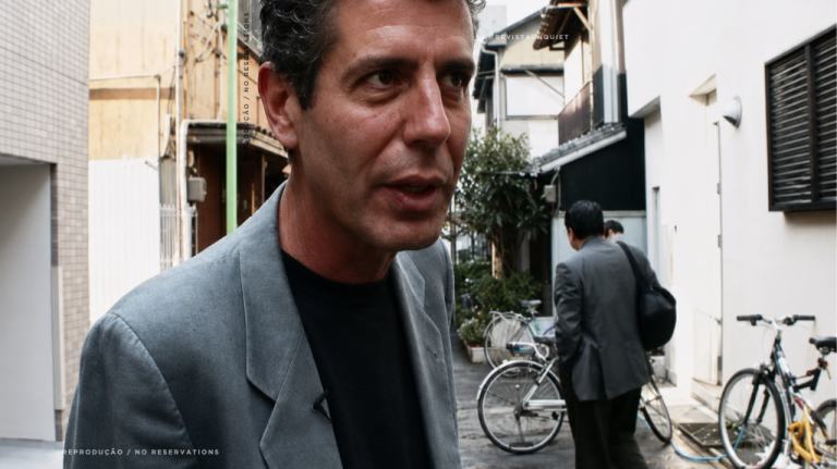 Foto mostra Anthony Bourdain em uma rua urbana de Tóquio, na região de Kantō, no Japão, em cena de viagem documental. A imagem sugere a densidade gastronômica japonesa, com referências a izakayas, yakitori, soba, ramen, sushi de balcão e turismo gastronômico no Japão. Anthony Bourdain na rua em Tóquio