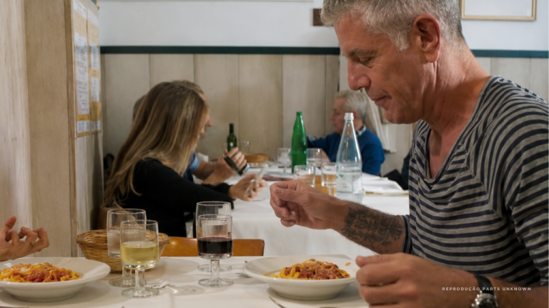 Anthony Bourdain comendo em uma mesa simples em Roma, capital da Itália, na região do Lácio, com ambiente de trattoria e refeição italiana cotidiana. A imagem remete à cozinha romana, à cacio e pepe, à carbonara, às trattorias de bairro e ao turismo gastronômico na Itália Anthony Bourdain comendo em uma mesa simples em Roma