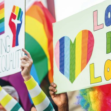 Participantes seguram cartazes e bandeiras do arco-íris em celebração do Orgulho LGBTQIA+, tema de artigo sobre Paradas LGBTQIA+ pelo mundo, visibilidade e luta por direitos.