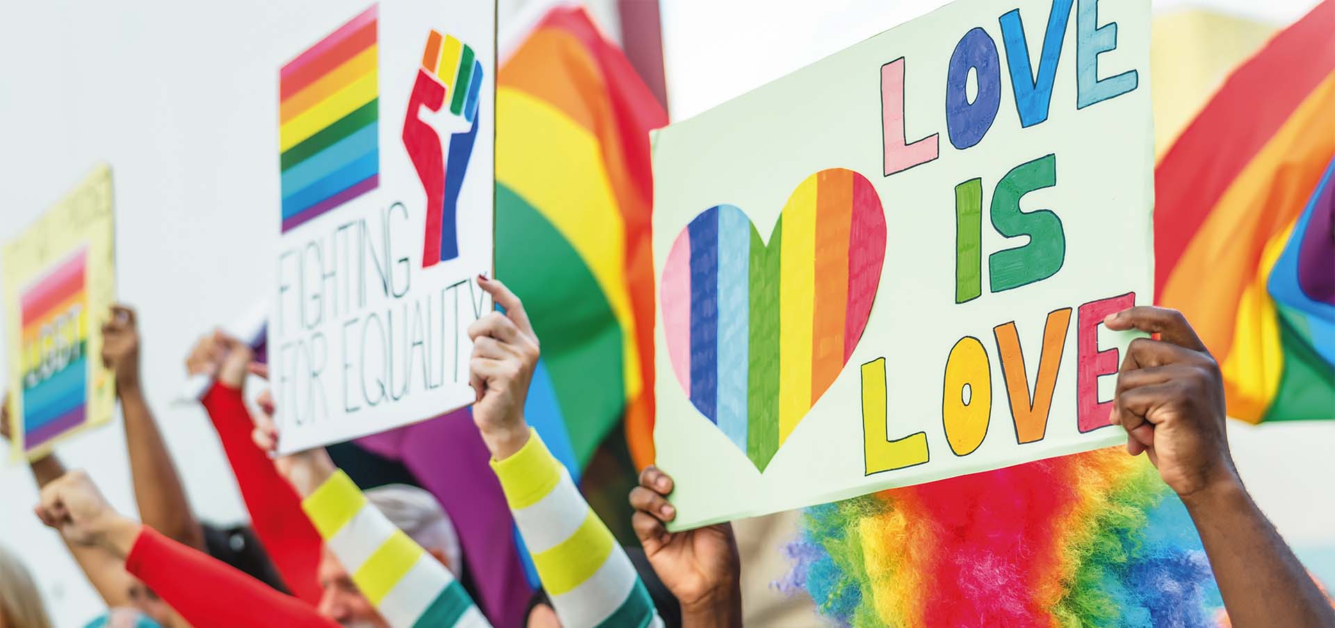 Participantes seguram cartazes e bandeiras do arco-íris em celebração do Orgulho LGBTQIA+, tema de artigo sobre Paradas LGBTQIA+ pelo mundo, visibilidade e luta por direitos.