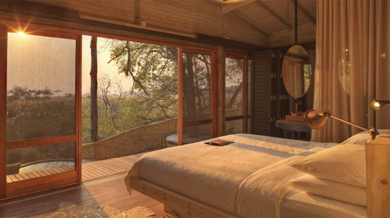 Suíte do &Beyond Sandibe Okavango Safari Lodge, no Delta do Okavango, no noroeste de Botsuana, com cama voltada para a savana, madeira, telas de proteção e design integrado à paisagem. Suíte do &Beyond Sandibe Okavango Safari Lodge, no Delta do Okavango, no noroeste de Botsuana, com cama voltada para a savana, madeira, telas de proteção e design integrado à paisagem.