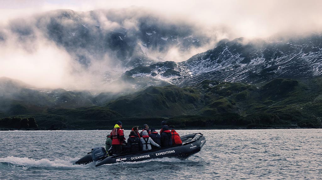 Bote zodiac navegando diante de montanhas nevadas na Geórgia do Sul, em cruzeiro de expedição pelo Atlântico Sul.