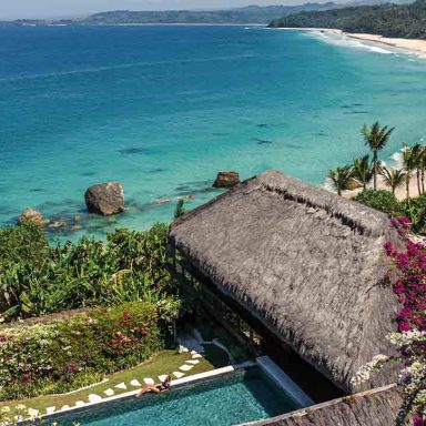 Vista aérea do Nihi Sumba, hotel de luxo na Ilha de Sumba, no leste da Indonésia, com villa de telhado tradicional, piscina privativa, jardins tropicais, praia preservada e mar azul-turquesa do Oceano Índico.