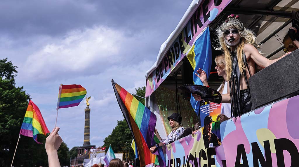 Participantes com bandeiras LGBTQIA+ em manifestação de rua durante celebração do Orgulho, com foco em visibilidade e direitos.