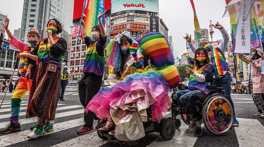 Participantes fantasiados em Parada LGBTQIA+ com bandeiras do arco-íris, em cena de celebração, ativismo e ocupação urbana.